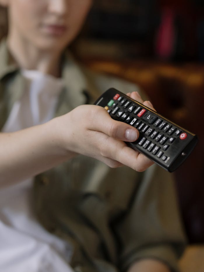 A person comfortably holding a television remote in a relaxed home environment, symbolizing leisure time.